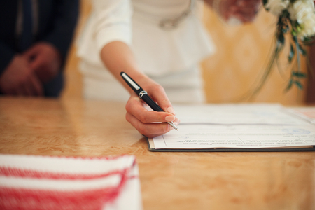 A closeup of delicate bride's hand while she signs wedding papersの写真素材