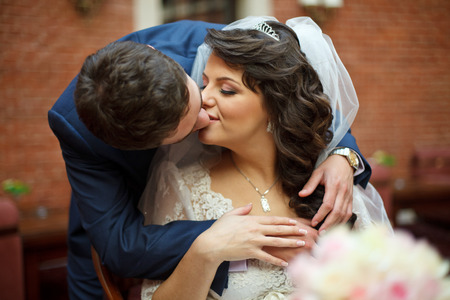 Groom kisses bride tenderly while she sits at the tableの写真素材