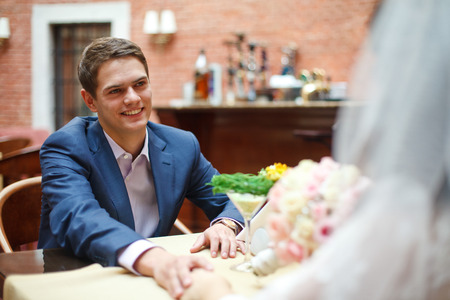 Handsome groom reaches his hand to a bride sitting at the tableの写真素材