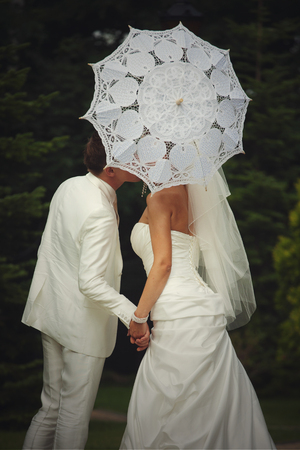 Bride hides her kiss behind a white umbrellaの写真素材