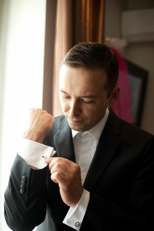 Groom adjusts the cufflinks standing in the light of morning sunの写真素材