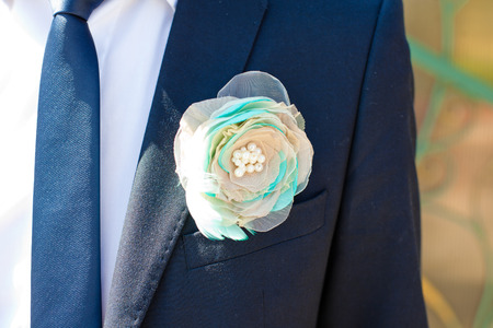 White boutonniere decorated with mint feathers pinned to blue jacket
