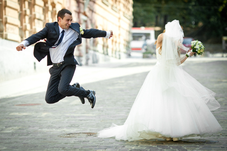 Bride hides under the veil while groom jumps around herの写真素材