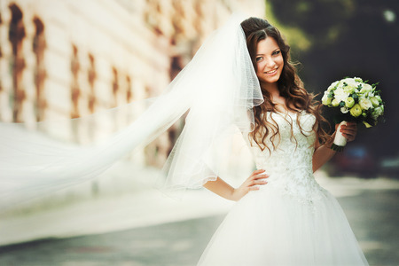 Smiling bride with bright face looks over her shoulder standing on the street in a sunny dayの写真素材