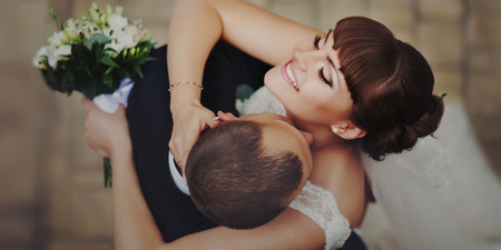 Groom kisses bride's shining skin hugging her tenderの写真素材
