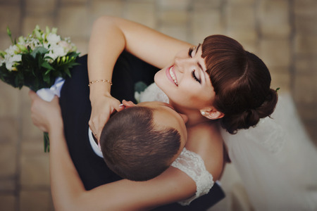 Bride clothes her eyes and smiles while groom kisses her neckの写真素材
