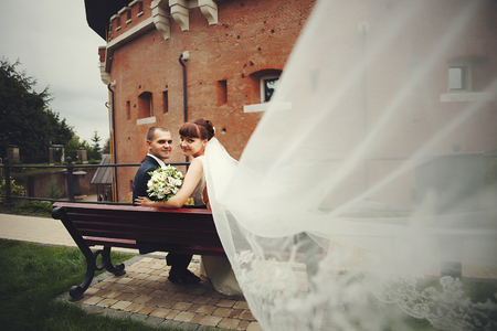 A look from bride's veil on the happy wedding couple sitting on the benchの写真素材
