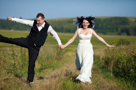 Wind blows bride's black curls while groom jumps behind herの写真素材