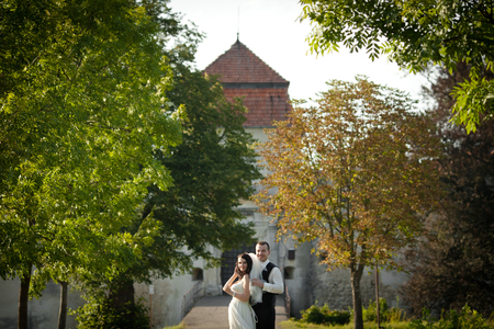 Groom holds bride's veil while standing behind her in the castle parkの写真素材