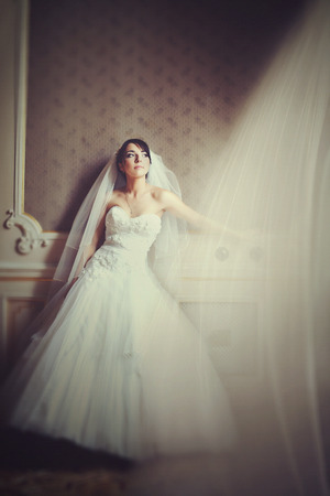 Wind blows white curtain on the window while bride leans to a wallの写真素材