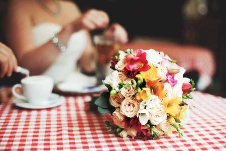 Wedding bouquet lies over the plaid tablecloth while bride drinks teaの写真素材