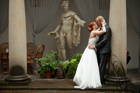 Bride and groom kiss standing before an old Greek statueの写真素材