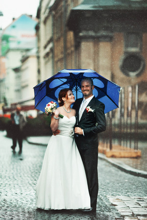 Happy newlyweds hide under the blue umbrellaの写真素材