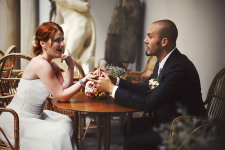 Bride tells something to a bald-headed groom sitting at the cafe tableの写真素材