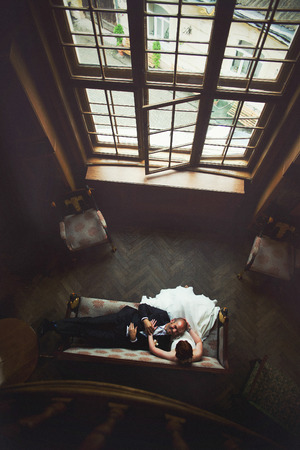 Wedding couple rests on the couch in the front of high windowの写真素材