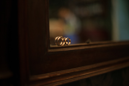 Tiny wedding rings stand on the frame of a mirror