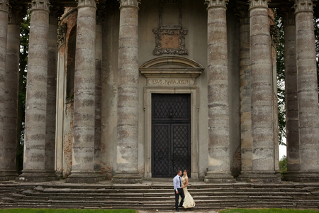 A look from afar on a young couple standing in the front of huge stone building surrounded with pillarsの写真素材