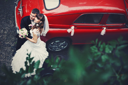 Wedding couple leans on a red car standing outsideの写真素材