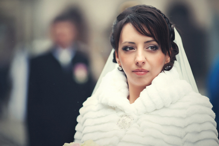 Gorgeous bride in fur coat stands thoughtful on the streetの写真素材