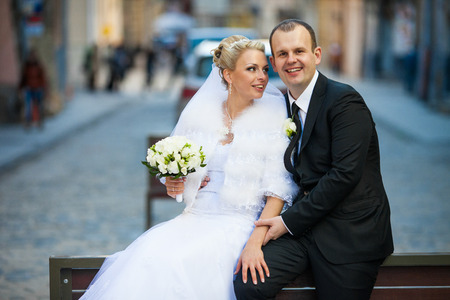 Bride leans to a groom while they sit on the back of a benchの写真素材