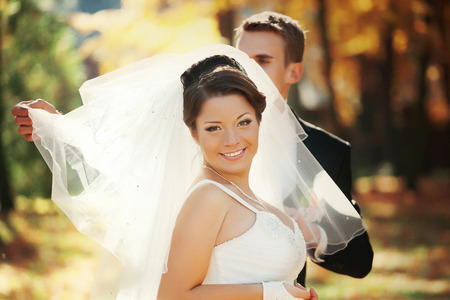 Groom spreads bride's veil while autumn sun shines through itの写真素材