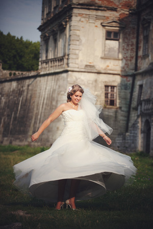 Blonde bride whirls on the green grass in the front of a castleの写真素材