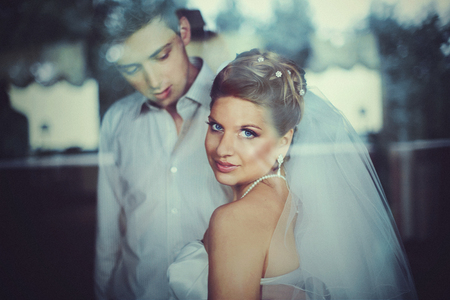 A look through the glass on a marvelous bride with blue eyes sitting behind a groomの写真素材