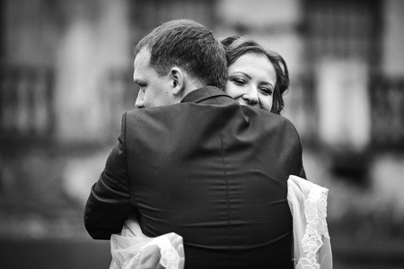 Bride holding veil in her hands hugs groom tenderの写真素材