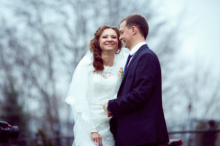 Happy wedding couple stands in a cold park covered with fogの写真素材