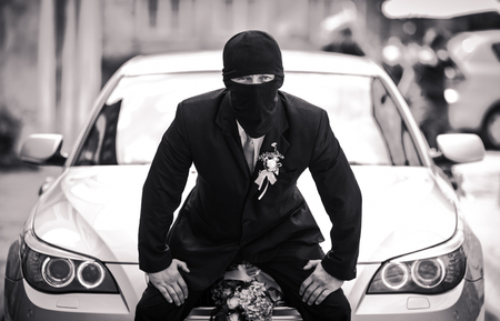 Groom dressed like a robber sits on the carの写真素材