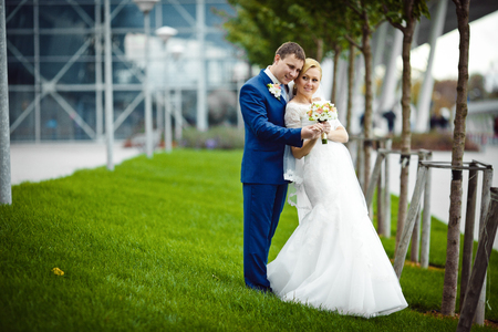 Beautiful wedding couple stands on the green grass in a cloudy summer dayの写真素材
