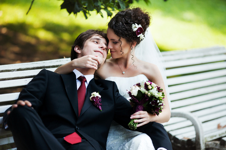 Groom rests on bride's shoulder while they sit on the benchの写真素材