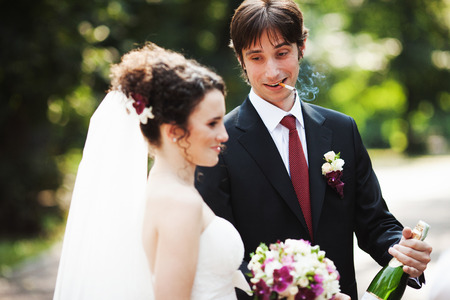 Smoking groom stands behind a bride with a bottle of champagneの写真素材