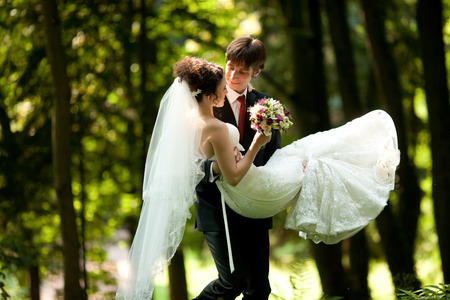 Groom carries a tiny bride on his hands walking through the forestの写真素材