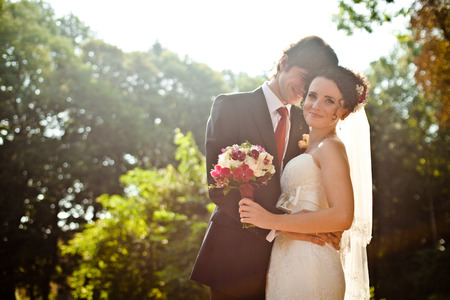 Groom hides his smile behind bride's head hugging her in the gardenの写真素材