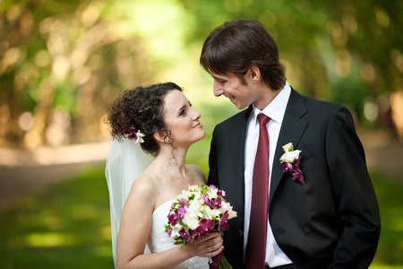 Stylish newlyweds in classy clothes with red details look at each otherの写真素材