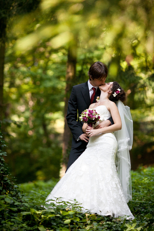 Fiance kisses a tiny bride standing in the forestの写真素材