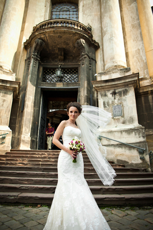 Wind blows a veil of curly bride while she stands behind an entrance to the old cathedralの写真素材