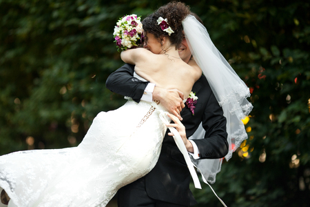 Bride's veil covers groom's face while he whirls her in the parkの写真素材