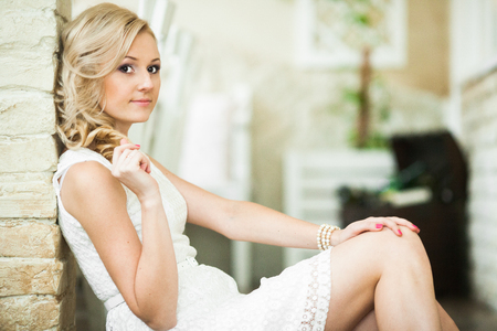 Beautiful blonde touches her curls while sitting on the floorの写真素材