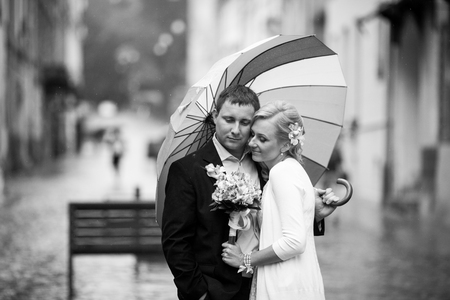 Daydreaming wedding couple enjoys a moment under the rain on the streetの写真素材