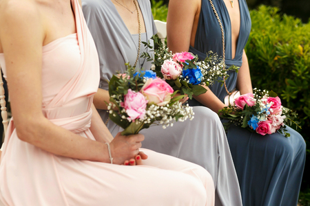 Pink wedding bouquets lie on the knees of bridesmaids in pastel dressesの写真素材