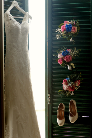 Sun shines through the green doors on which hang dress, shoes and bouquetsの写真素材