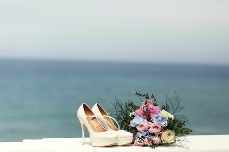 Classy white shoes on high heels stand on the white handrails with great view on the sea behind themの写真素材