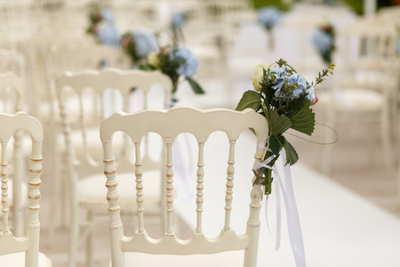 Bouquets of greenery and blue hydrangeas pinned to the white chairsの写真素材