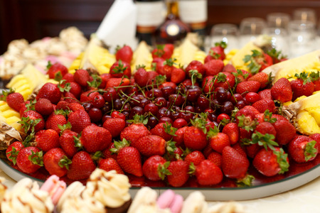 Red cherries lie in the middle of plate served with strawberries and ananasの写真素材