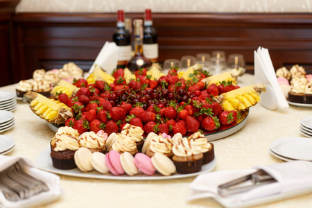 Fruits and pink sweets stand served on the table covered with white clothの写真素材