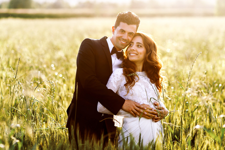 Happy bride leans to groom's shoulder while posing in the fieldの写真素材
