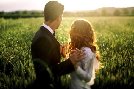 Bride and groom watch the sunset over the field holding their hands togetherの写真素材