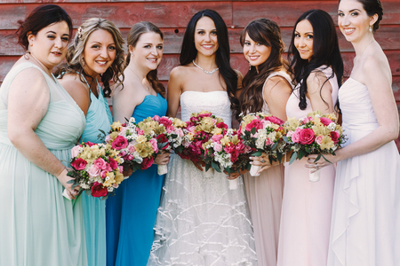 Attractive bridesmaids surround a pretty bride while posing before a wooden hangarの写真素材